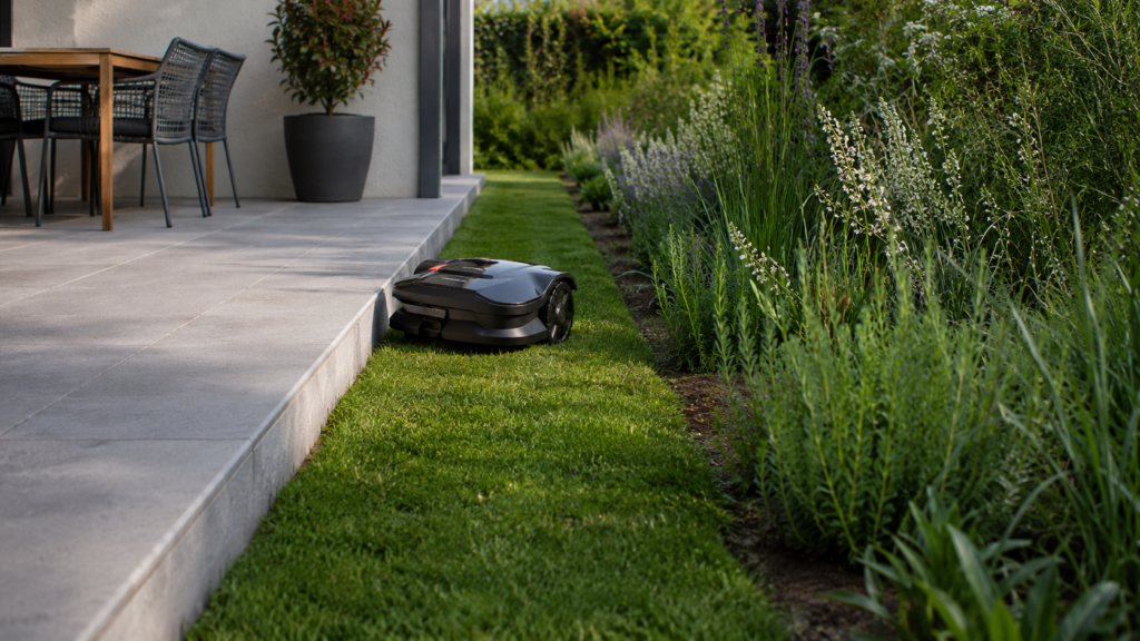 Mähroboter an sauberer befahrbarer Rasenkante neben Terrasse und Staudenbeet